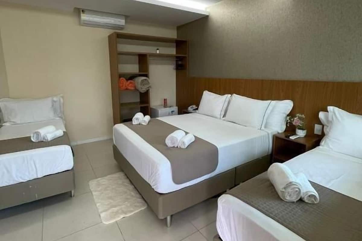 A hotel room with two single beds, a larger bed, and a small table. There is a closet with shelves and a mirror.