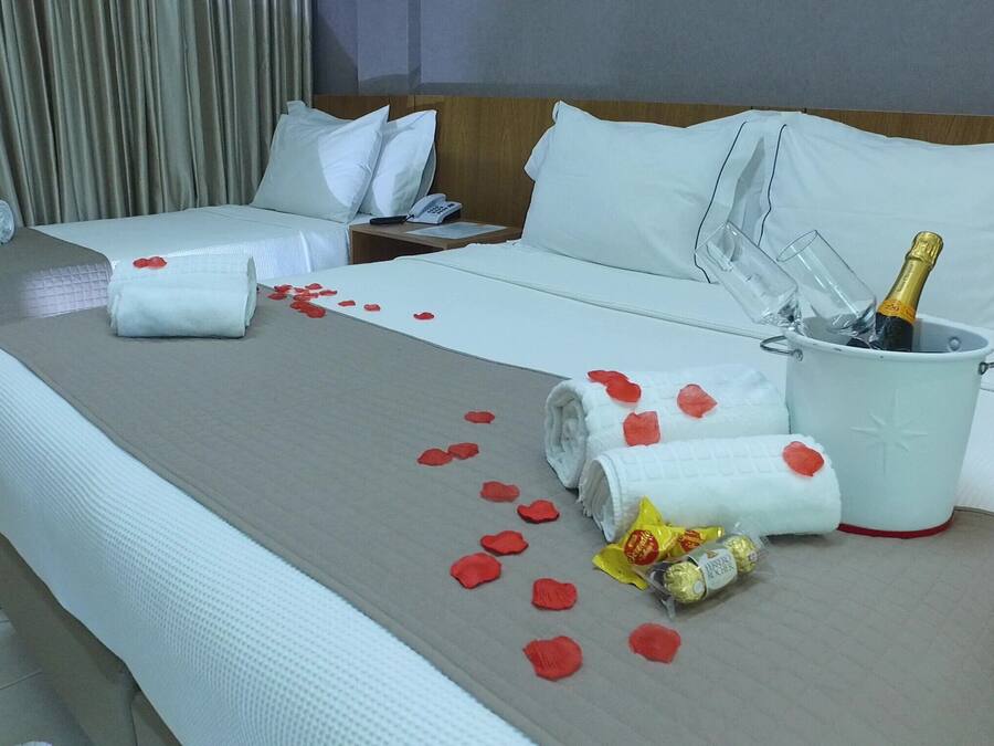 Habitació d'hotel amb un llit, una taula de nit i pètals de roses al llit, juntament amb una ampolla de xampany.
