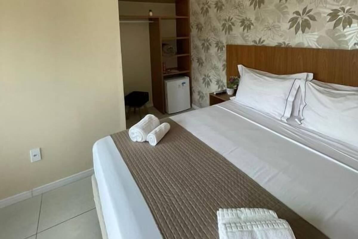 A hotel room with a bed, a wardrobe, a small desk, and an air conditioning unit.