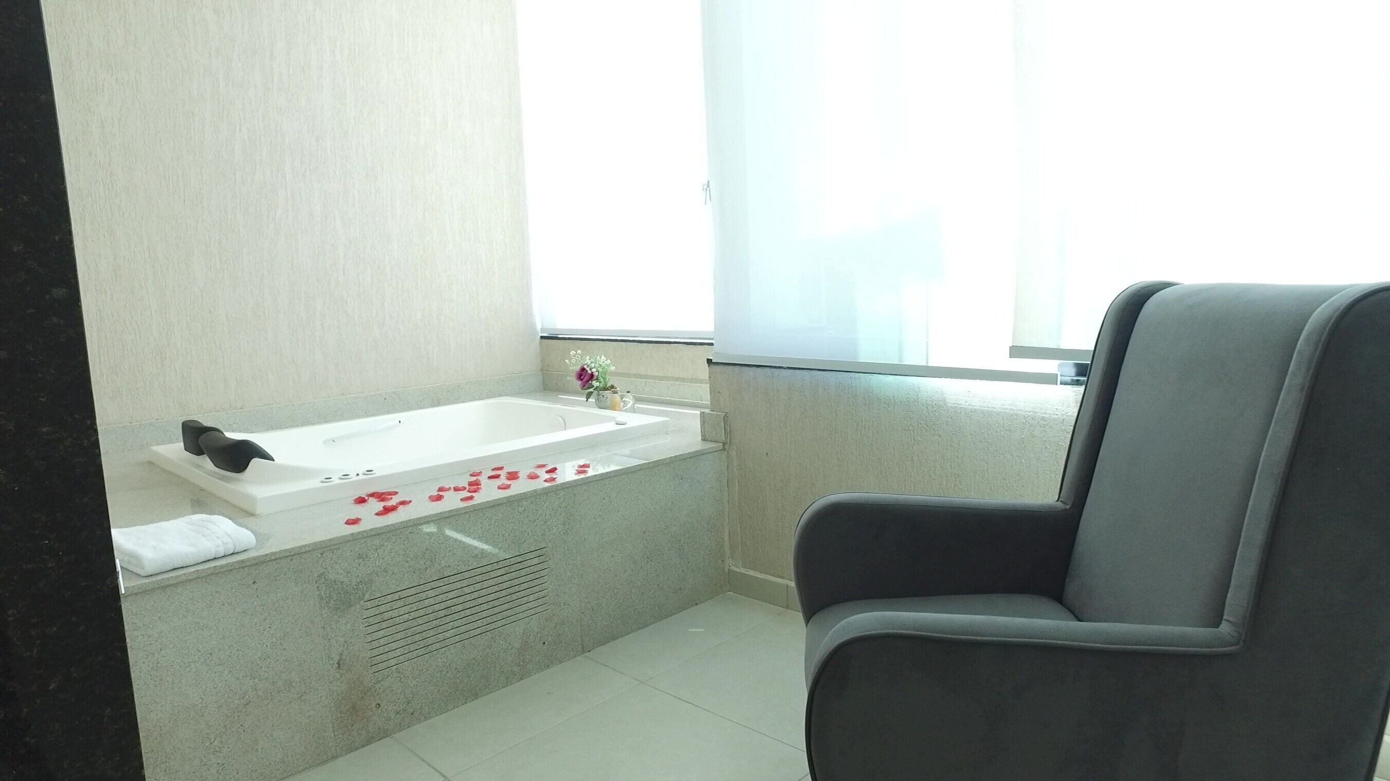 A bathroom with a bathtub, a window, and a chair.