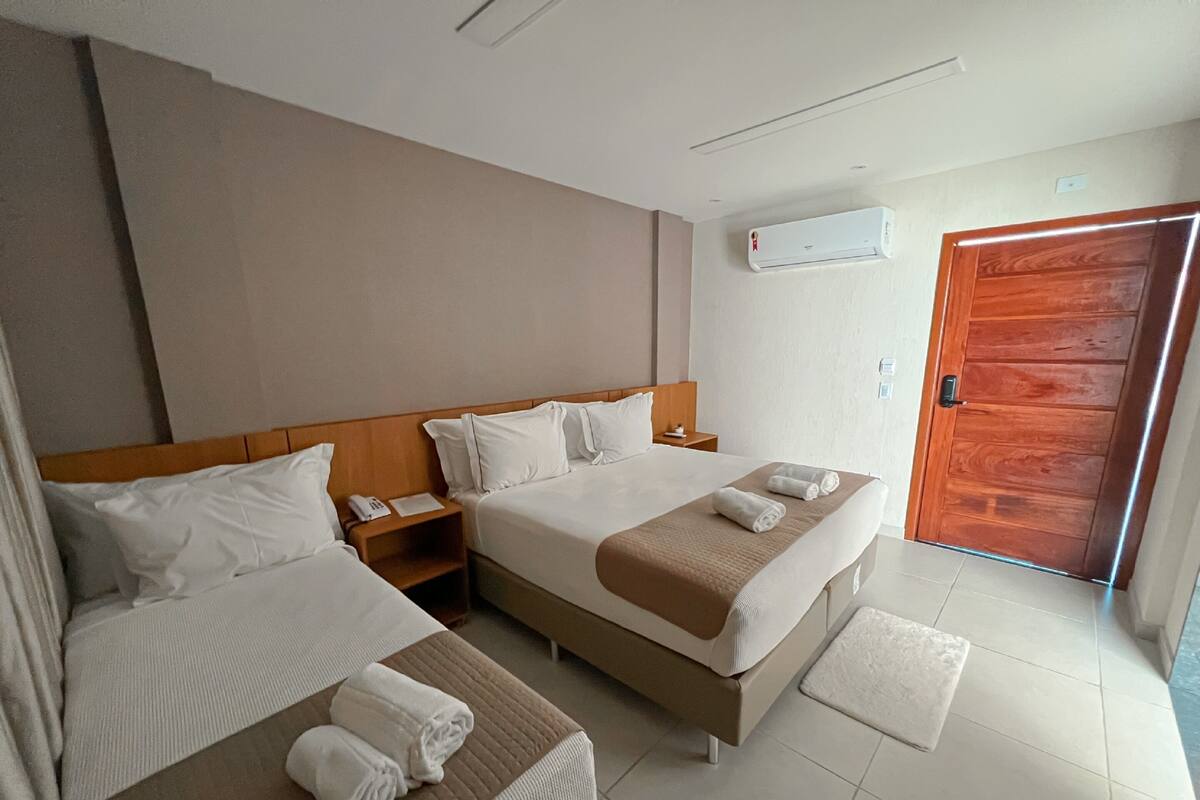 A hotel room with two beds, a wooden headboard, a bedside table with a phone, a wall-mounted air conditioner, and a wooden door.