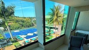 A balcony with a jacuzzi, a chair, and a view of a pool and greenery. -  Viver Pousada (Saquarema)