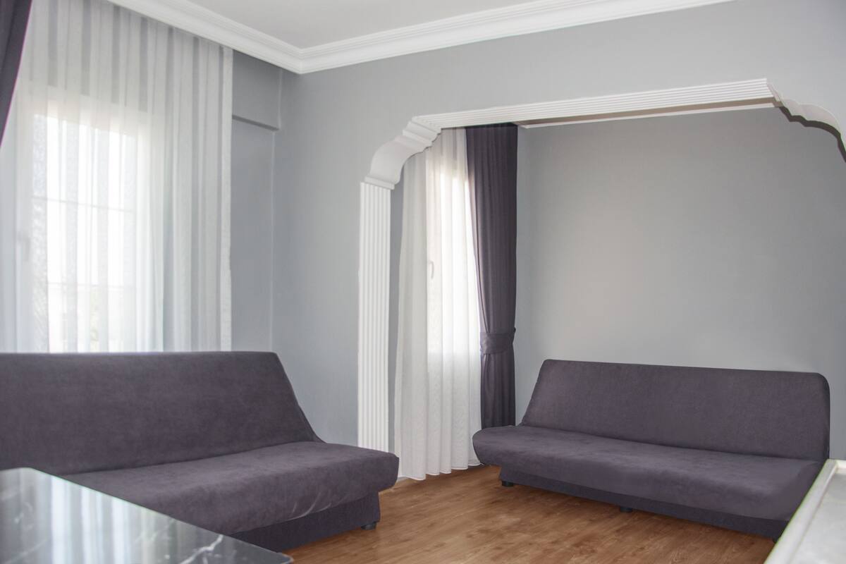 Um quarto com dois sofás cinzentos, uma mesa de vidro e piso de madeira.