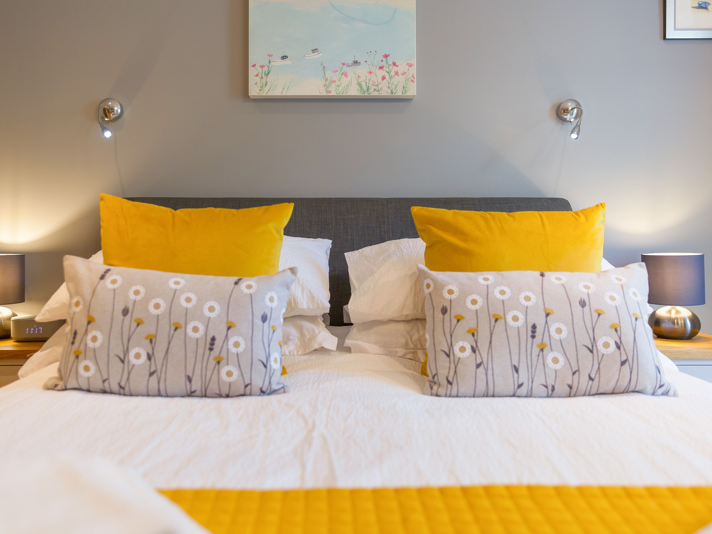 A neatly made bed with white and yellow bedding, two yellow pillows, and a floral-patterned pillow.