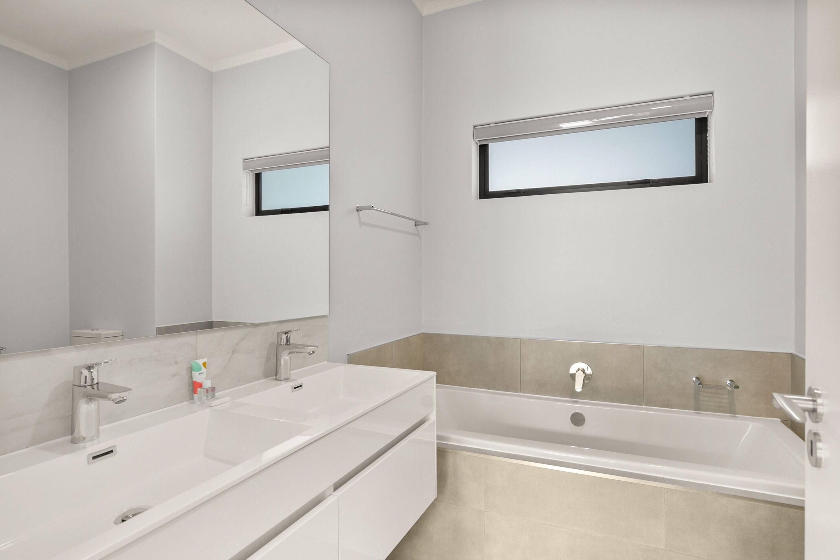 Un baño moderno con un espejo grande, lavamanos doble, bañera y toallero.