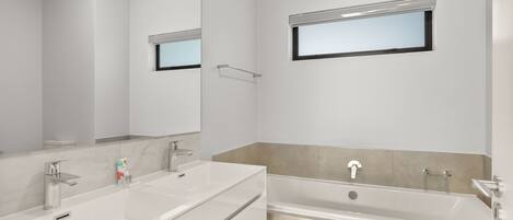 Un baño moderno con un espejo grande, lavamanos doble, bañera y toallero.