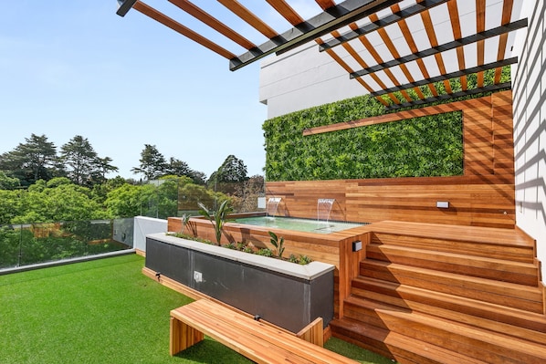 Une terrasse extérieure moderne, dotée d’une plateforme en bois, d’un jardin intégré agrémenté de plantes et d’une petite fontaine.