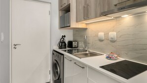 A compact kitchen with a washing machine, a kettle, a toaster, and a sink.