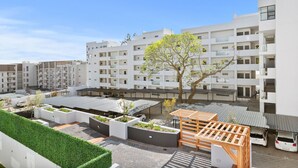 A modern apartment complex with multiple balconies, a central courtyard with greenery, and a clear blue sky.
