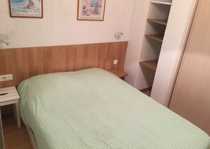 Quarto com cama, mesa de cabeceira, cabeceira de madeira, prateleira na parede e porta.
