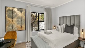 Une chambre moderne avec un grand lit, une table de chevet, une chaise et une grande fenêtre avec des rideaux.