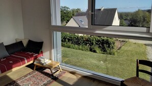 A room with a large window, a bed with a red cover, a small table, and a chair. - House between Morgat beach (2km) and Crozon town (1km). (Crozon)