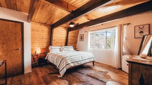 Ein gemütliches Zimmer mit Holzbalkendecke, einem Bett mit gemusterten Textilien, einem Fenster mit Vorhängen und einem Lederteppich auf dem Boden.