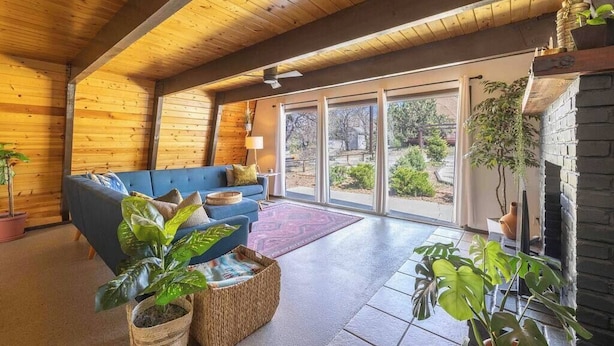Ein gemütliches Zimmer mit blauem Sofa, Holzboden und großen Fenstern mit Blick ins Freie.