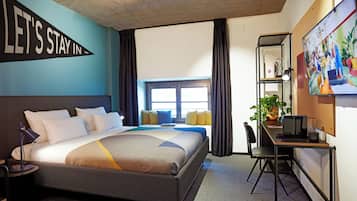 Habitación de hotel con cama, escritorio, computadora, silla, ventana con cortinas y un letrero grande en la pared.