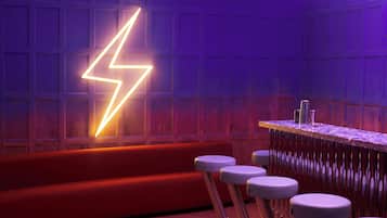 Un área de bar con un letrero de neón con forma de rayo, un sofá rojo y taburetes de bar.