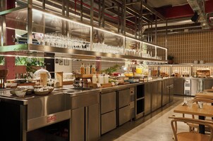 A modern kitchen with stainless steel appliances, a service counter, and a seating area with wooden tables and chairs.