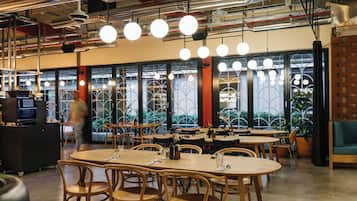 A modern restaurant interior with round tables, wooden chairs, hanging pendant lights, and large windows with decorative ironwork.