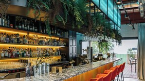 A bar area with a marble countertop, multiple shelves of liquor bottles, and orange bar stools. - The Social Hub Madrid 4 star (Madrid)