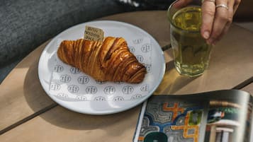 A croissant on a plate with a label, a glass of yellow liquid, and a magazine on a table.