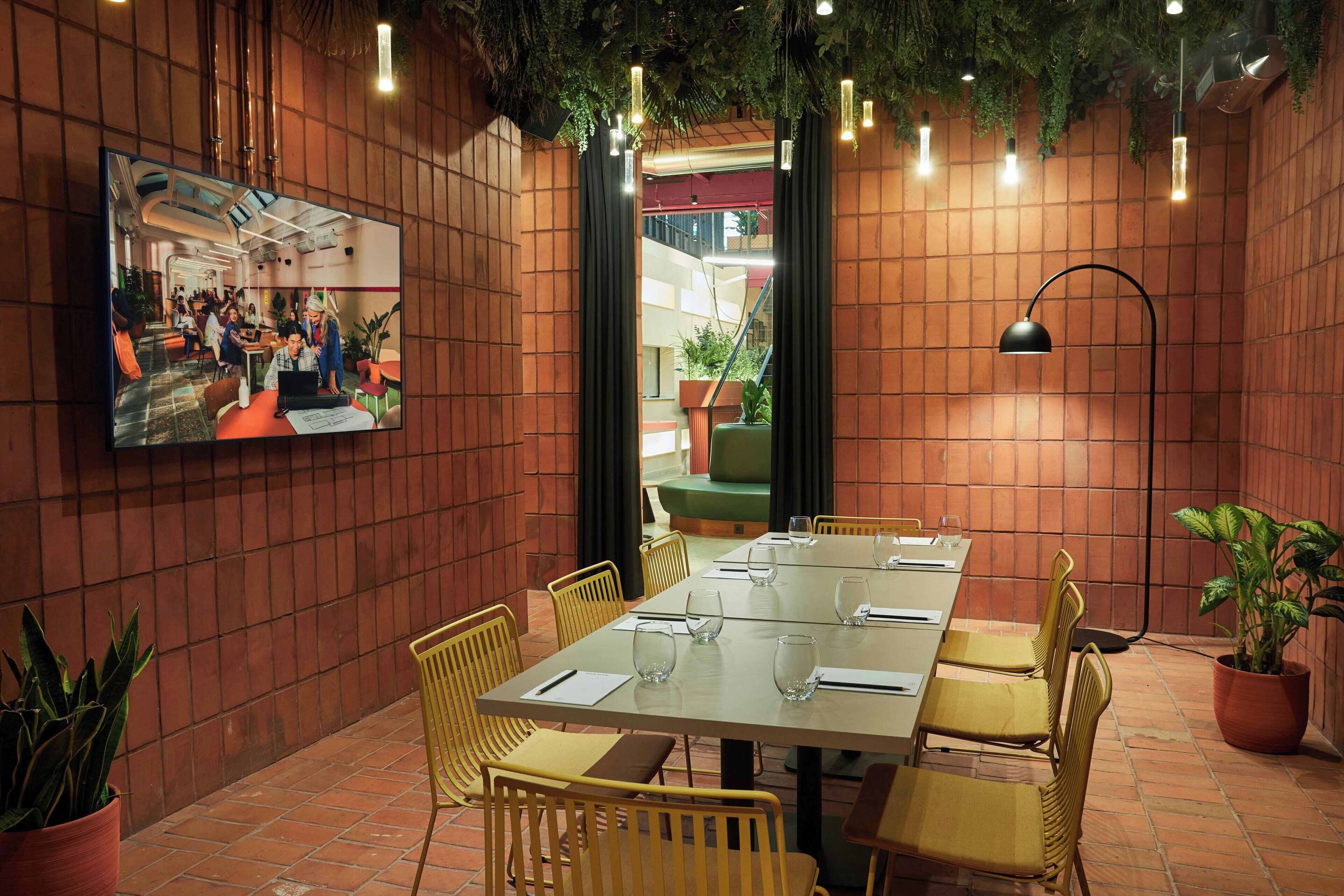 A conference room with a long table, yellow chairs, a TV on the wall, and potted plants.