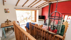 A spacious living area with a wooden staircase, a dining table, and a television. - Lime Kiln Cottage (Bridgend)