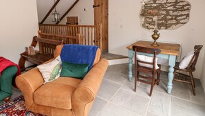 A cozy living room with a brown sofa, a wooden dining table, and a stone wall. - Lime Kiln Cottage (Bridgend)