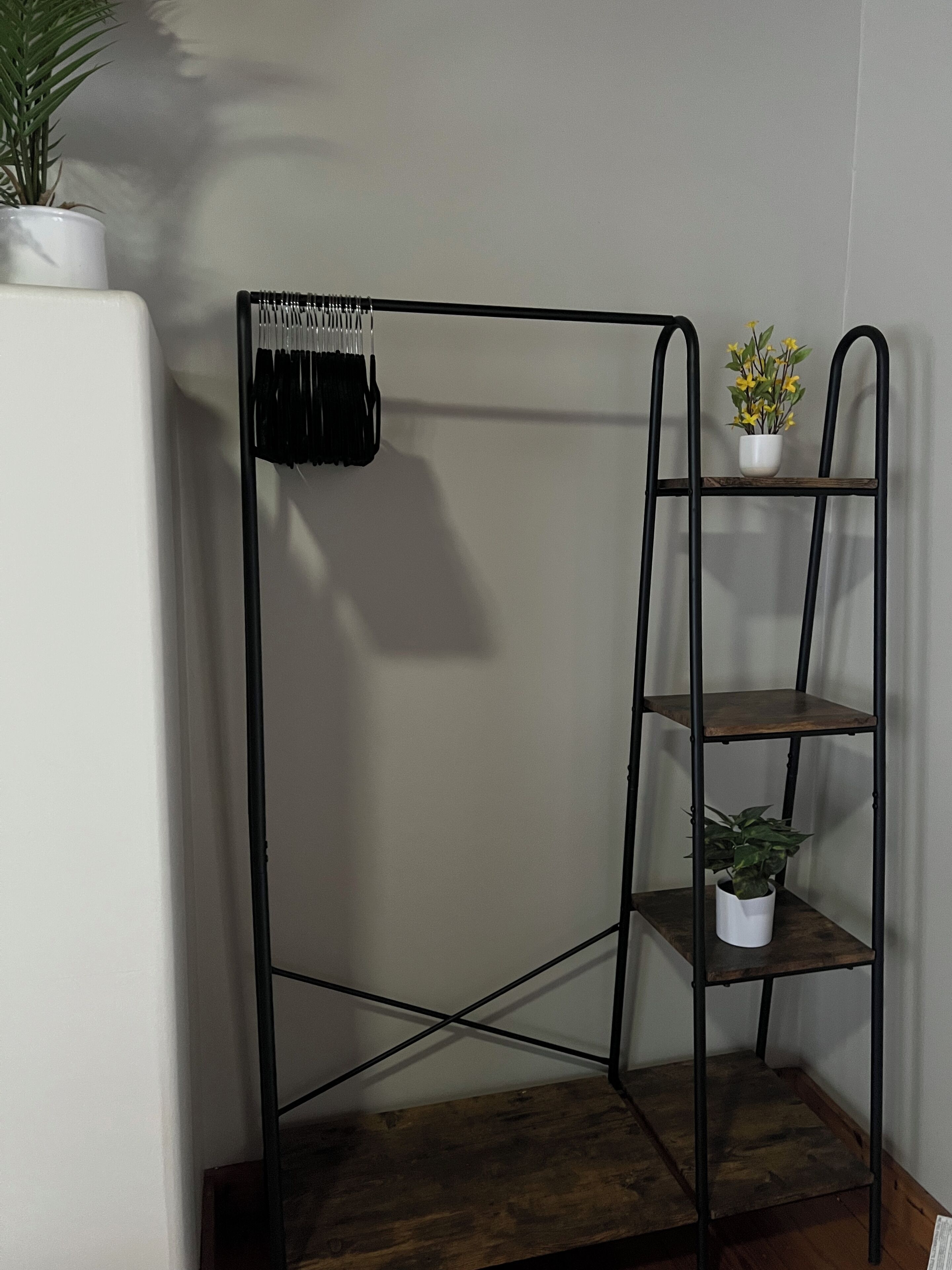 Une pièce d’angle avec une étagère en métal, une plante en pot et un mur blanc.
