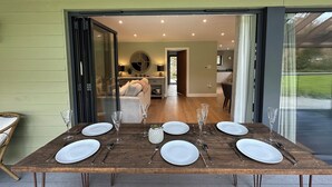 A dining table set with plates, cutlery, and glasses, with a view of a kitchen and living area in the background. - Primrose (Bodmin)