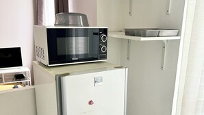 A compact kitchen with a white refrigerator, a microwave on top, and a small shelf above.