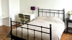 A bedroom with a bed, a desk, a chair, and a nightstand.