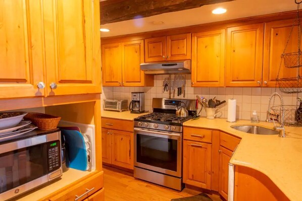 A kitchen with wooden cabinets, a stove, a microwave, and a sink. - Village Home with 15 acre backyard on the river (Cavendish)