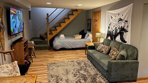 A cozy living room with a sofa, a TV, a staircase, and a bed. - Village Home with 15 acre backyard on the river (Cavendish)