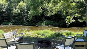 A riverside seating area with wooden chairs and a fire pit. - Village Home with 15 acre backyard on the river (Cavendish)