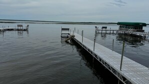 A calm water body with a dock extending into it, featuring a covered seating area and a small boat.