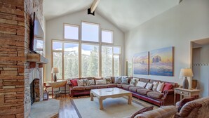 Un salón espacioso con chimenea de piedra, ventanas amplias, un sofá modular y una mesa de centro.