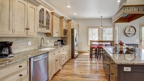 Una cocina con armarios de madera, un refrigerador de acero inoxidable, una encimera de granito y un comedor con una silla roja.