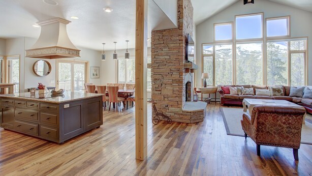 Amplia sala de estar con chimenea de piedra, piso de madera y ventanas grandes que ofrecen vistas al exterior.