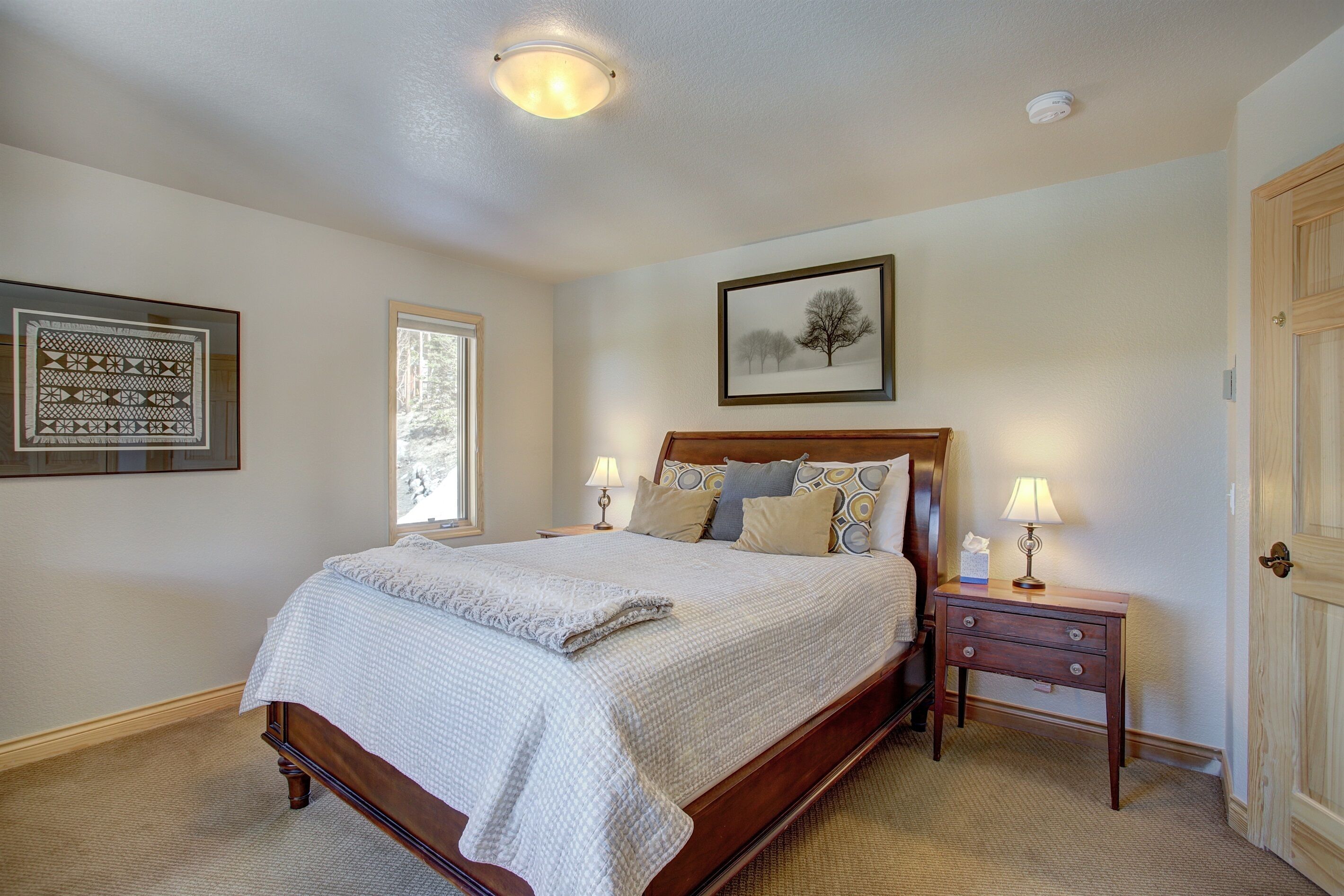 A bedroom with a large bed, a nightstand with a lamp, a framed picture on the wall, and a door.