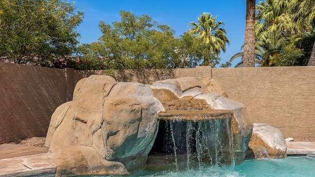 Zwembad met waterval, omgeven door grote rotsen en palmbomen.