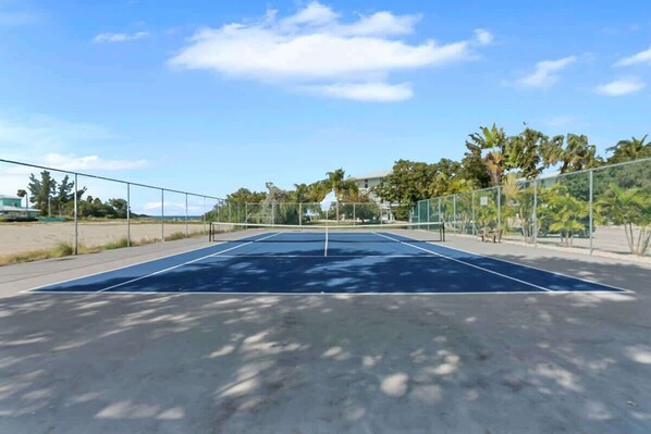 An outdoor tennis court with a net, surrounded by trees and a clear sky. - Gulf-Front Condo, Pool & Dock | Marathon, FL (Marathon)