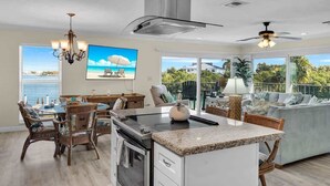A spacious kitchen with a central island, dining area with wicker chairs, and a large window overlooking a scenic view.