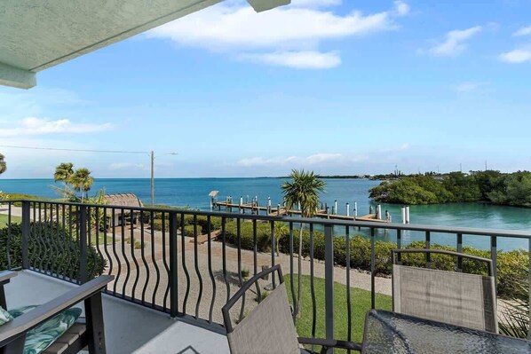 Un balcon offrant une vue sur une étendue d’eau paisible, un quai et une végétation luxuriante.