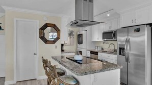 A modern kitchen with a central island, stainless steel appliances, and a hexagonal mirror.