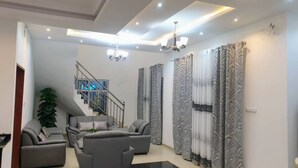 A modern living room with grey sofas, a staircase, and patterned curtains. - Magnificent house in quiet residential area (Yaoundé)