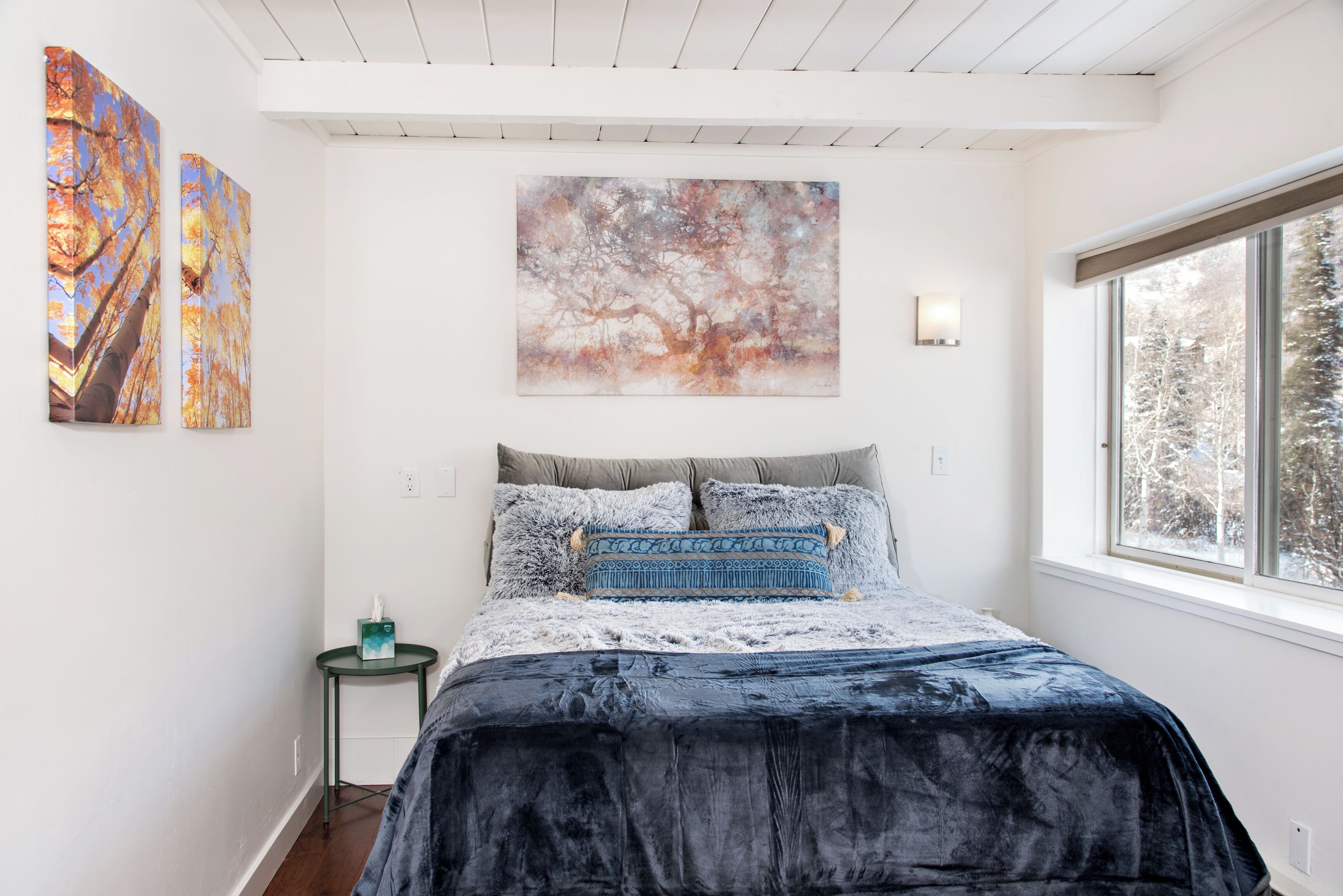 Une chambre avec un grand lit, une fenêtre et deux tableaux accrochés au mur.