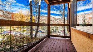 A wooden deck with a metal railing, overlooking a parking area and trees with autumn foliage. - Willows Condos by Snowmass Vacations (Snowmass Village)