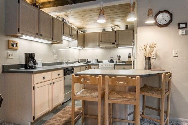 A kitchen with wooden cabinets, a central island with chairs, a stove, and a clock on the wall. - Willows Condos by Snowmass Vacations (Snowmass Village)