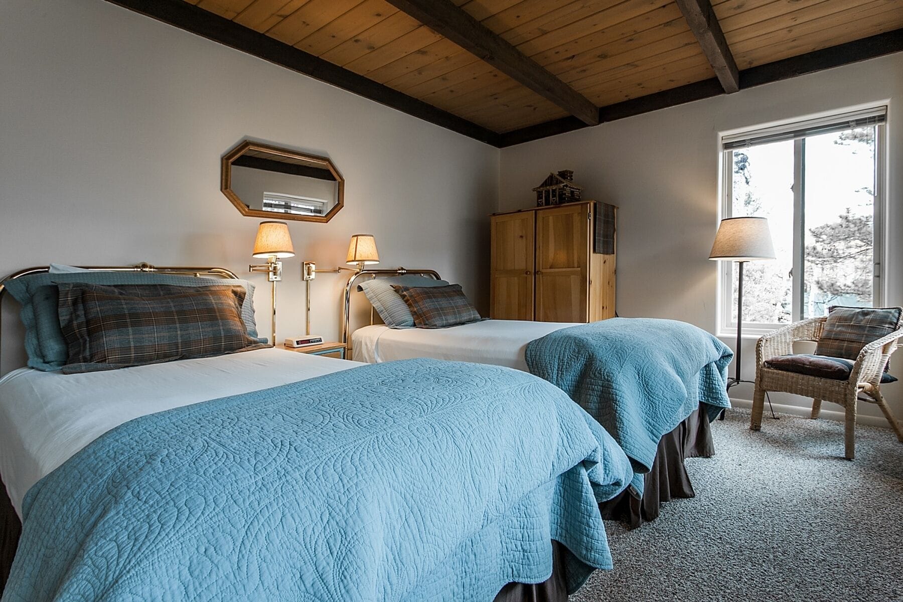A hotel room with two beds, a wooden wardrobe, a chair, and a large window.