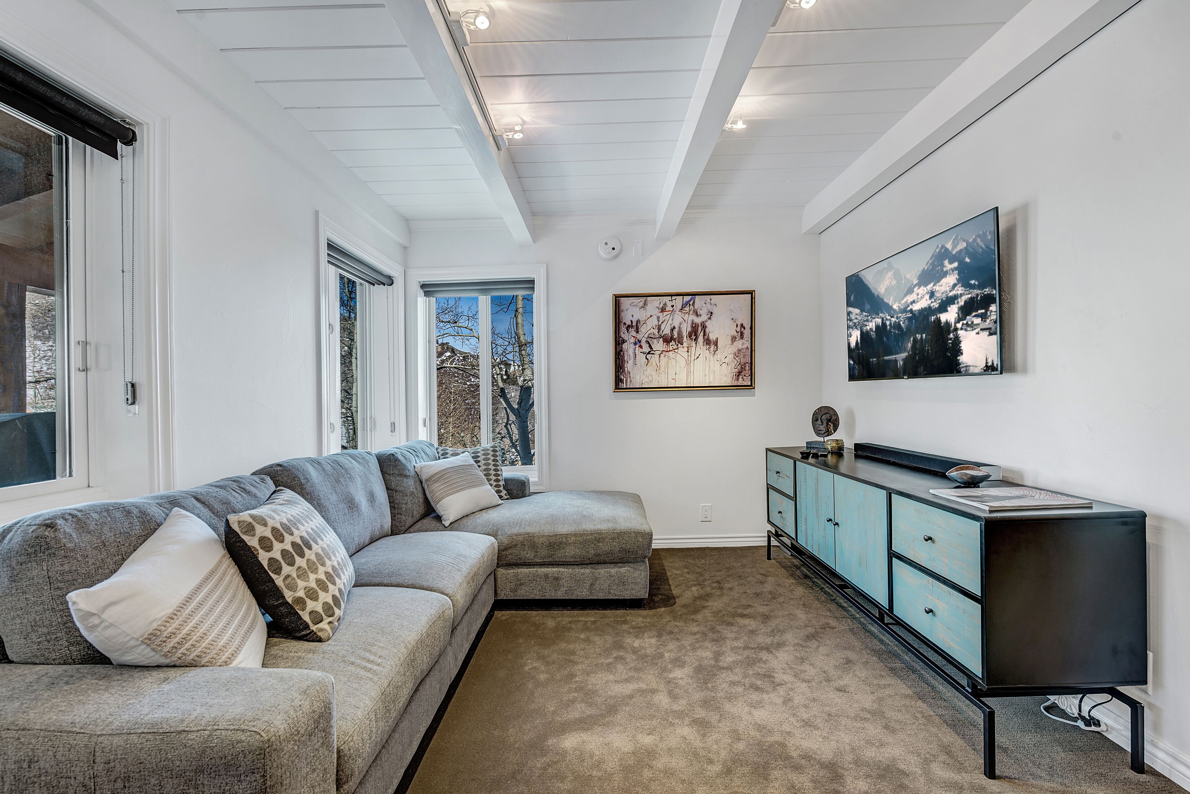 Ein modernes Wohnzimmer mit einem Ecksofa, einer hellblauen Kommode und einem großen gerahmten Bild an der Wand.